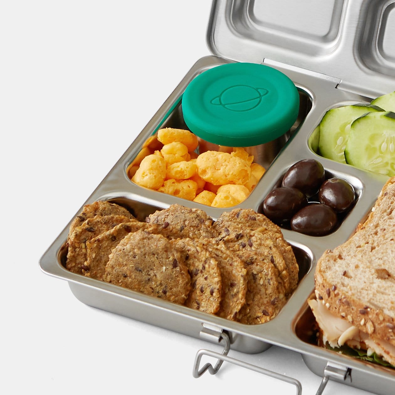Little Dipper container positioned within Rover lunchbox filled with crackers, cheese puffs, cucumbers, chocolate covered nuts and turkey sandwich.